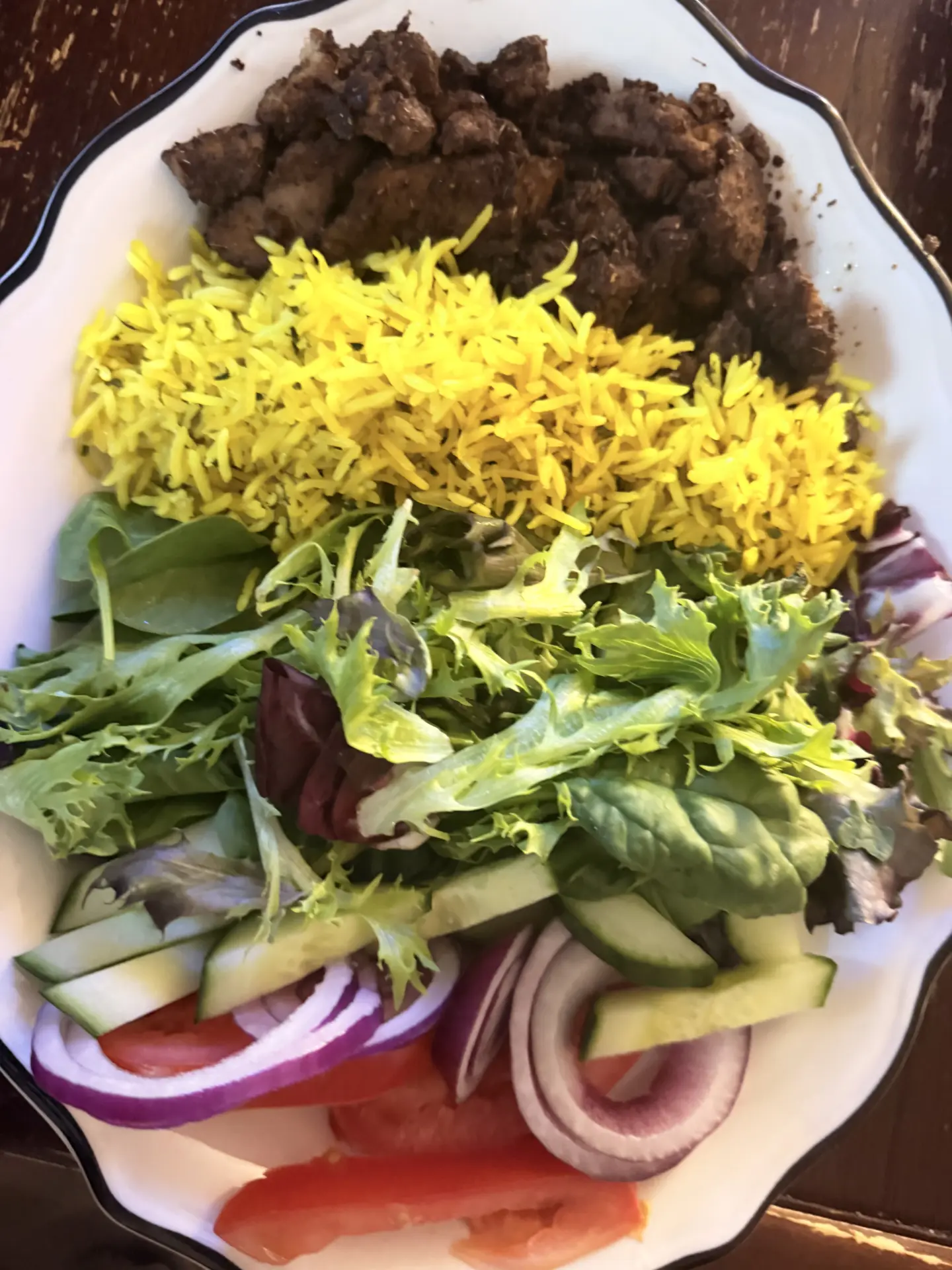 Bowl with yellow rice, seasoned protein and fresh salad greens